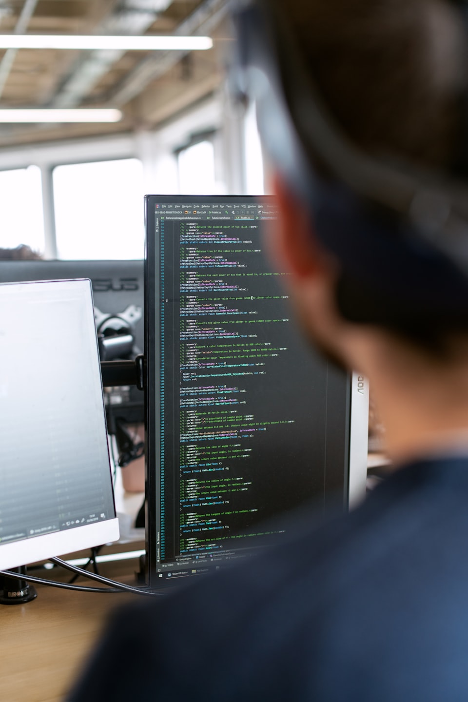 Programador concentrado en código en dos monitores de computadora.